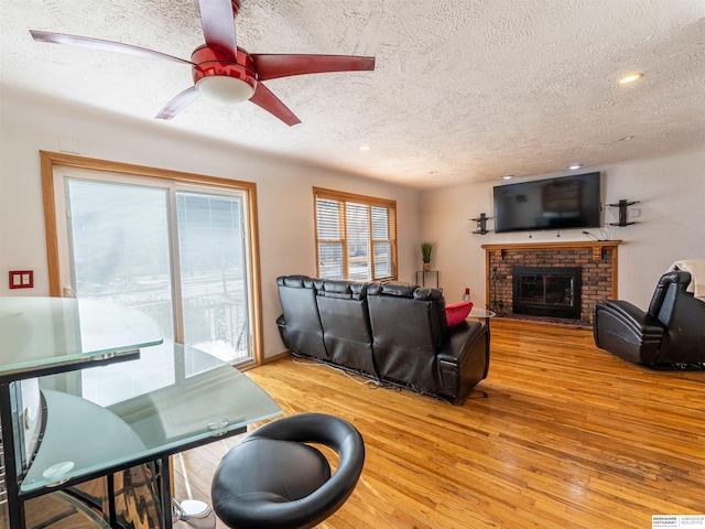 living area featuring a textured ceiling, a brick fireplace, and light wood-style floors