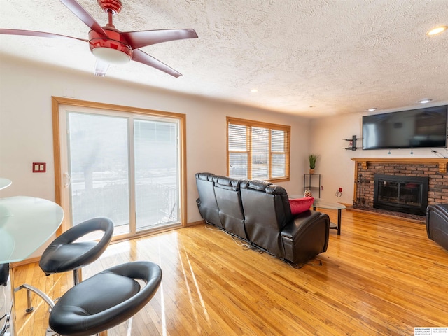 living area with light wood-style floors, a brick fireplace, ceiling fan, and a textured ceiling