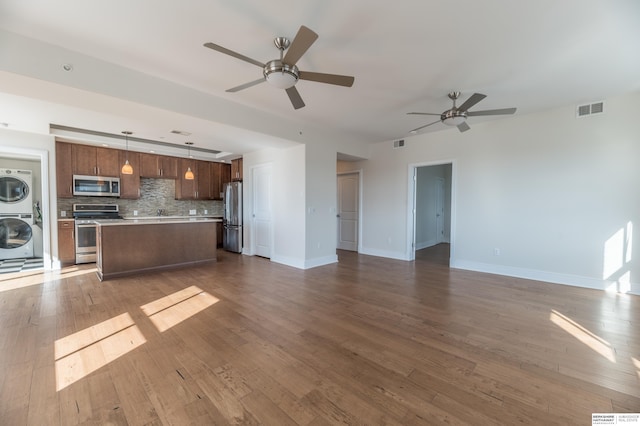 interior space with stainless steel appliances, stacked washer / dryer, open floor plan, hanging light fixtures, and light countertops