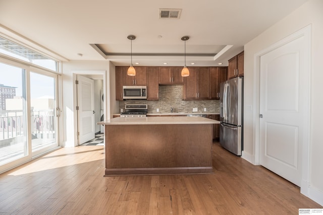 kitchen with appliances with stainless steel finishes, light countertops, a raised ceiling, and pendant lighting