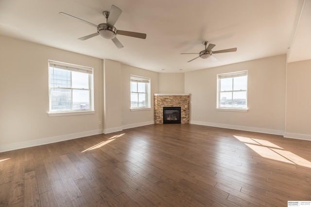 unfurnished living room featuring ceiling fan, a fireplace, dark wood finished floors, and baseboards