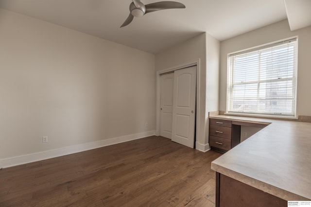 unfurnished office with dark wood-type flooring, a ceiling fan, and baseboards