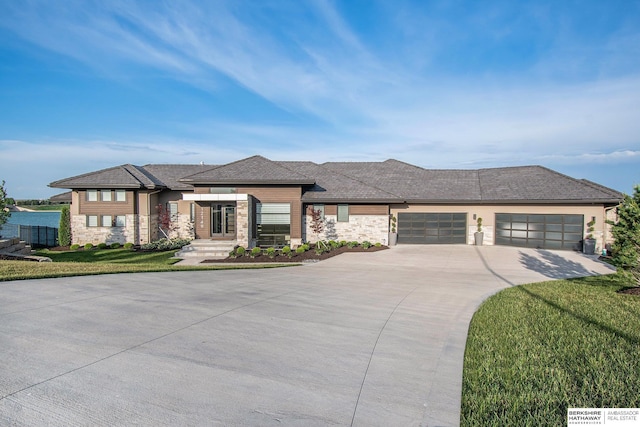 prairie-style home with a garage, concrete driveway, stone siding, and a front yard