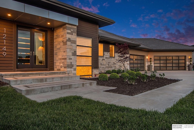 exterior entry at dusk with a garage and stone siding