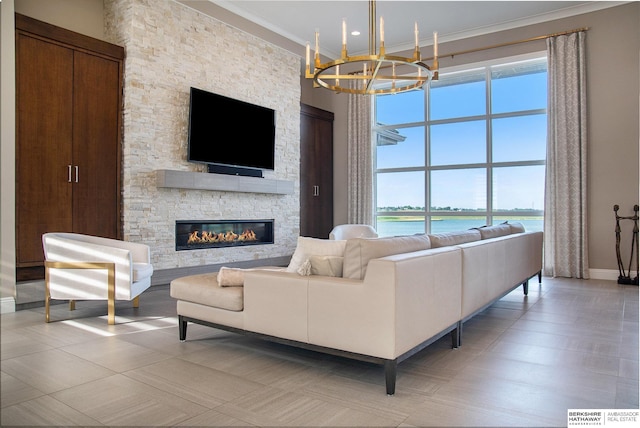 living room featuring baseboards, a towering ceiling, an inviting chandelier, crown molding, and a stone fireplace