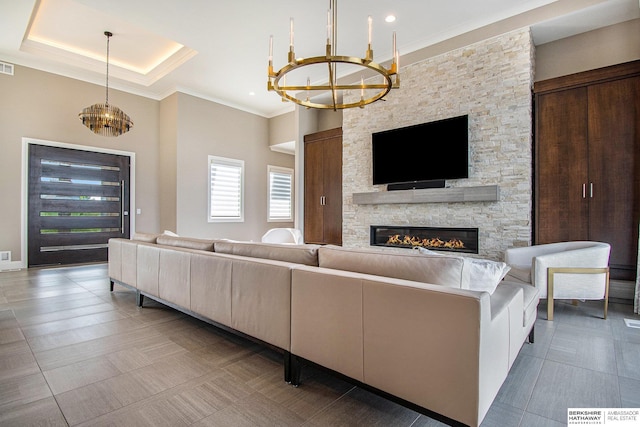 living room with visible vents, a tray ceiling, crown molding, a stone fireplace, and a chandelier