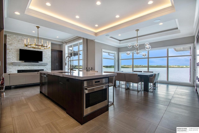 kitchen with a chandelier, oven, a kitchen island with sink, and a raised ceiling