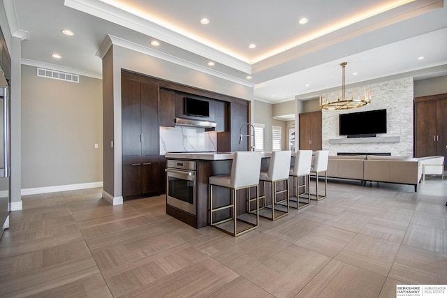 kitchen featuring visible vents, open floor plan, decorative light fixtures, a kitchen island with sink, and stainless steel oven