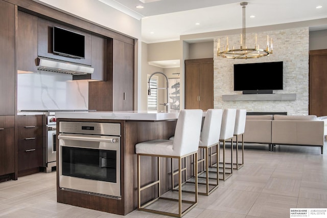 kitchen with range hood, light countertops, hanging light fixtures, open floor plan, and oven