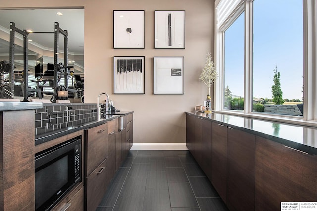 bar with black microwave, a sink, crown molding, and baseboards