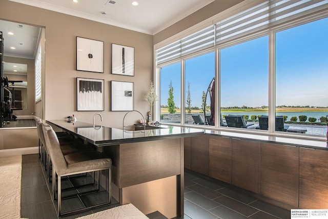 kitchen featuring a water view, dark countertops, modern cabinets, a kitchen bar, and crown molding