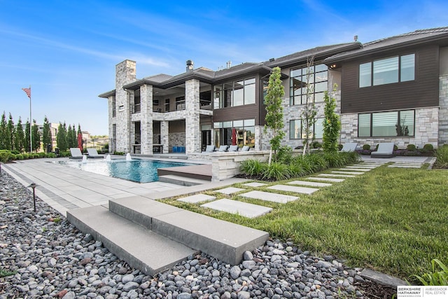 back of property with stone siding, a patio area, a chimney, and an outdoor pool