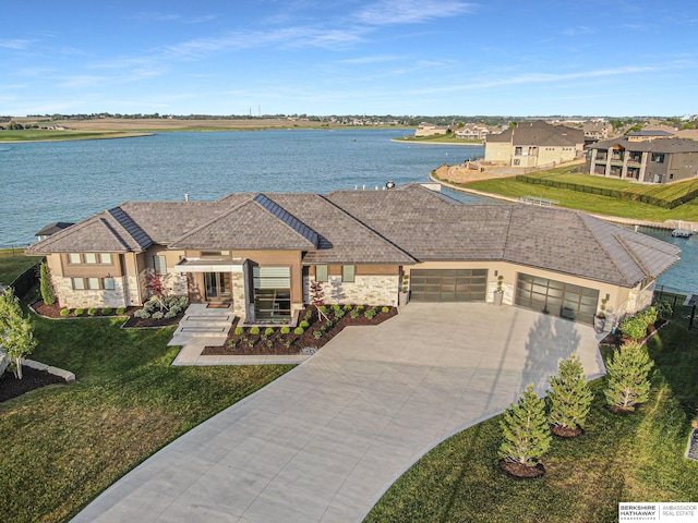 view of front facade featuring a garage, concrete driveway, stone siding, a water view, and a front lawn