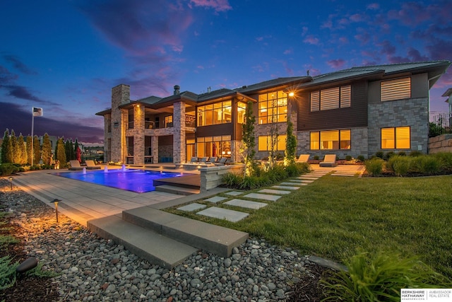 back of property with an outdoor pool, a patio, stone siding, a chimney, and a yard