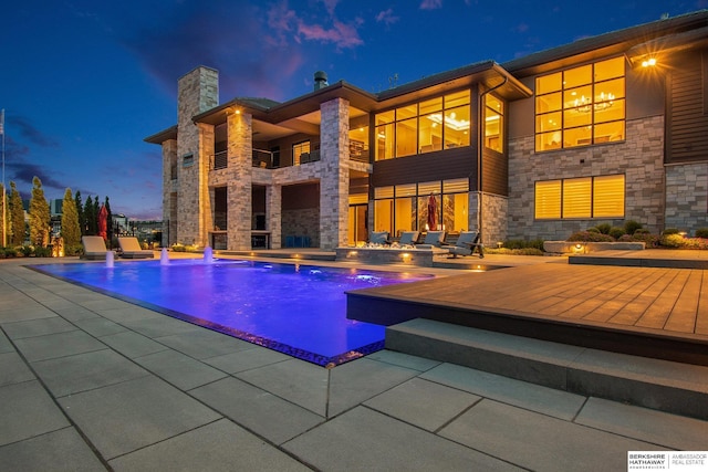 pool at dusk with an outdoor pool and a patio