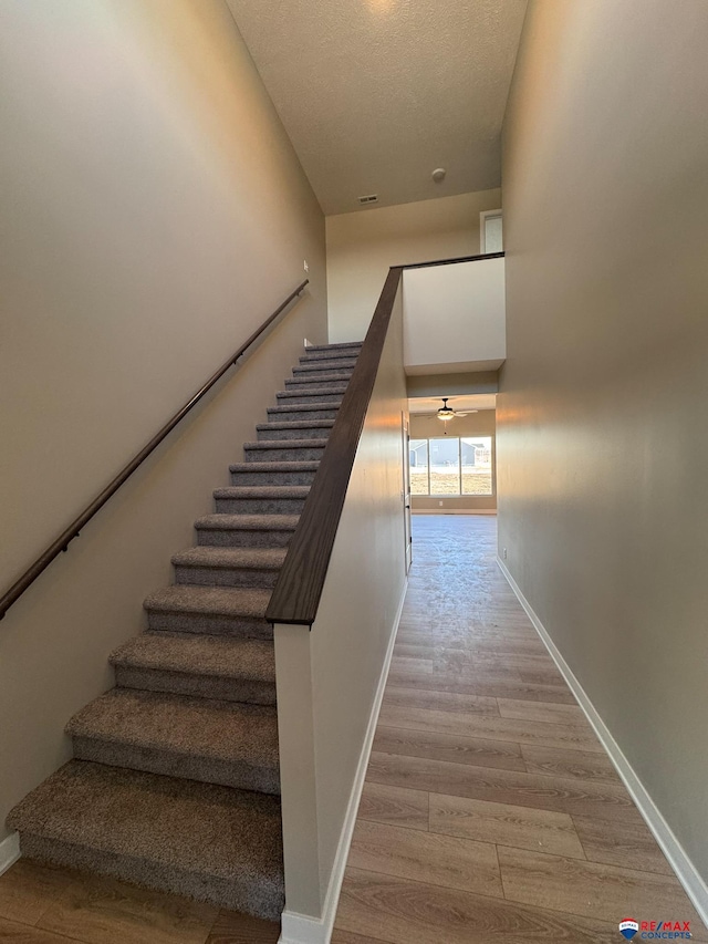 stairs with a textured ceiling, wood finished floors, and baseboards