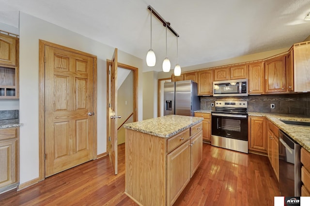 kitchen with tasteful backsplash, a kitchen island, hanging light fixtures, light stone countertops, and stainless steel appliances