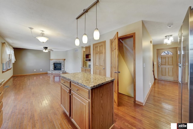 kitchen with a center island, pendant lighting, a brick fireplace, open floor plan, and light wood-type flooring