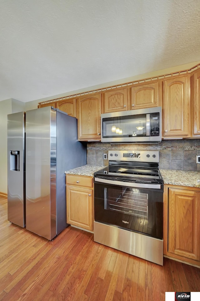 kitchen with light wood-style flooring, appliances with stainless steel finishes, tasteful backsplash, and light stone counters