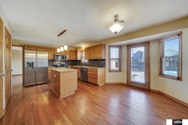 kitchen with tasteful backsplash, appliances with stainless steel finishes, decorative light fixtures, a center island, and a sink