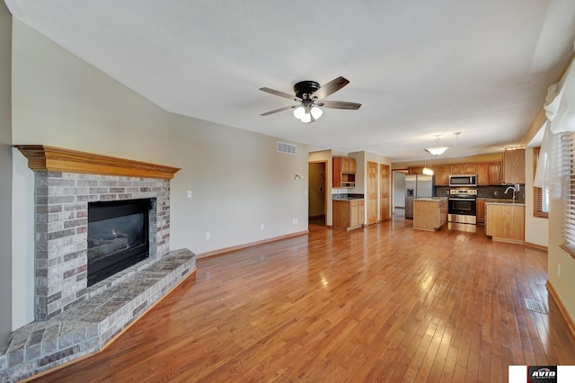 unfurnished living room with a fireplace, light wood finished floors, visible vents, a sink, and ceiling fan