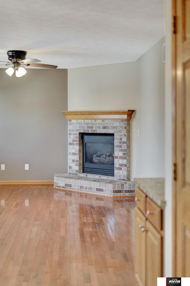 unfurnished living room featuring baseboards, ceiling fan, a fireplace, and light wood-style floors