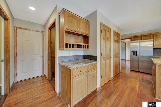 kitchen with light stone counters, light wood finished floors, stainless steel fridge with ice dispenser, and open shelves