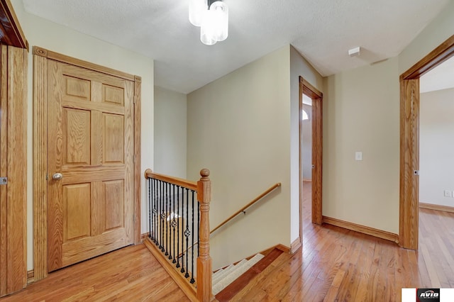 hall featuring baseboards, light wood-style flooring, an upstairs landing, and a textured ceiling