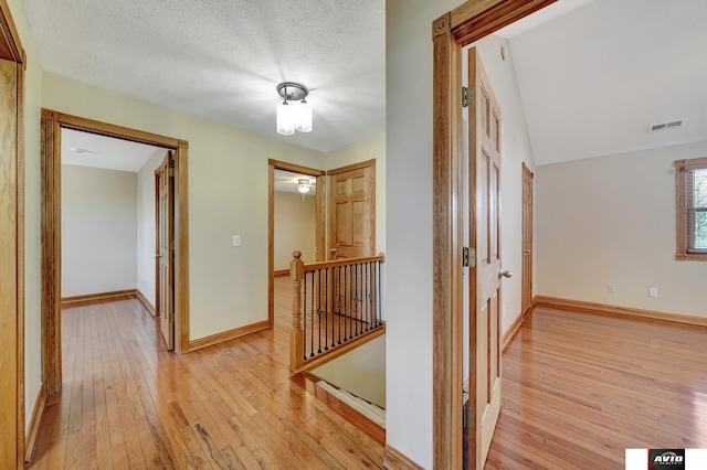 hallway with light wood-style floors, baseboards, visible vents, and an upstairs landing