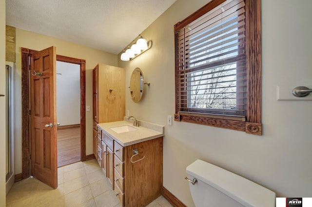 bathroom featuring toilet, vanity, a textured ceiling, baseboards, and tile patterned floors