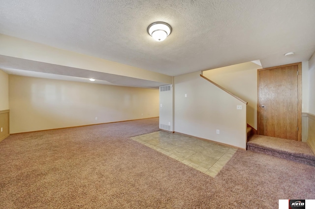 finished basement featuring visible vents, light colored carpet, a textured ceiling, baseboards, and stairs