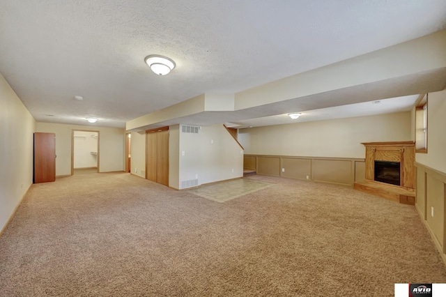 finished basement featuring visible vents, a glass covered fireplace, a textured ceiling, and light colored carpet