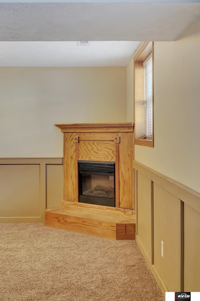 unfurnished living room with a wainscoted wall, carpet, and a glass covered fireplace