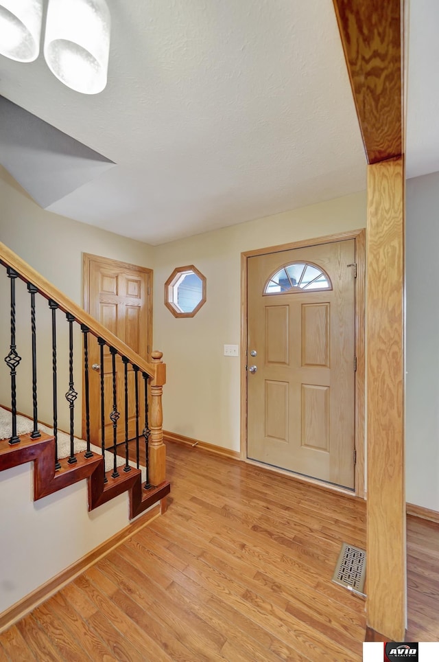 foyer entrance with stairway, wood finished floors, visible vents, and baseboards