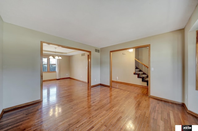 spare room with wood-type flooring, a raised ceiling, visible vents, and baseboards