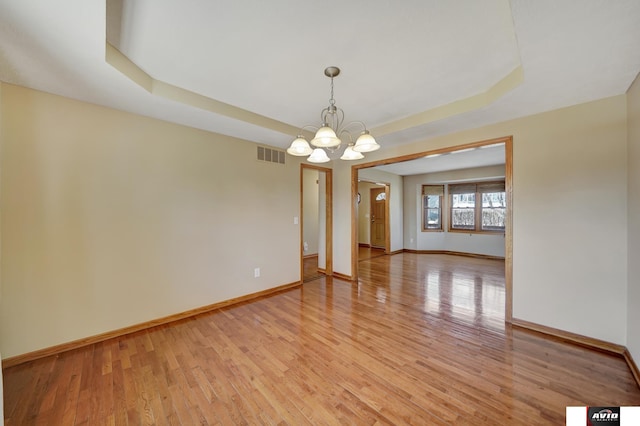 empty room with light wood-style flooring, a notable chandelier, visible vents, baseboards, and a raised ceiling