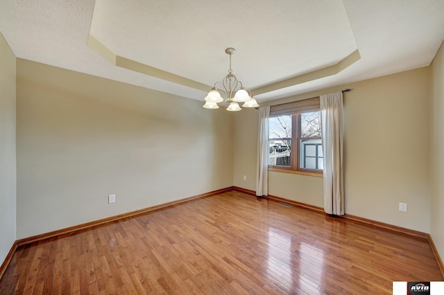 empty room with light wood-type flooring, a raised ceiling, visible vents, and baseboards