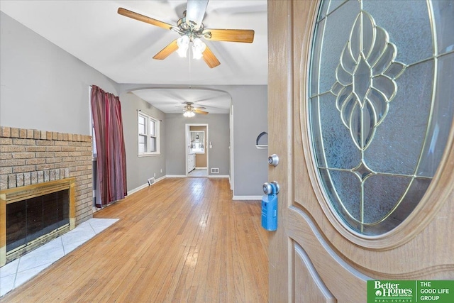 foyer with ceiling fan, arched walkways, a fireplace, baseboards, and hardwood / wood-style floors