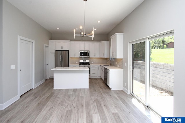 kitchen with white cabinets, a kitchen island, appliances with stainless steel finishes, light countertops, and pendant lighting