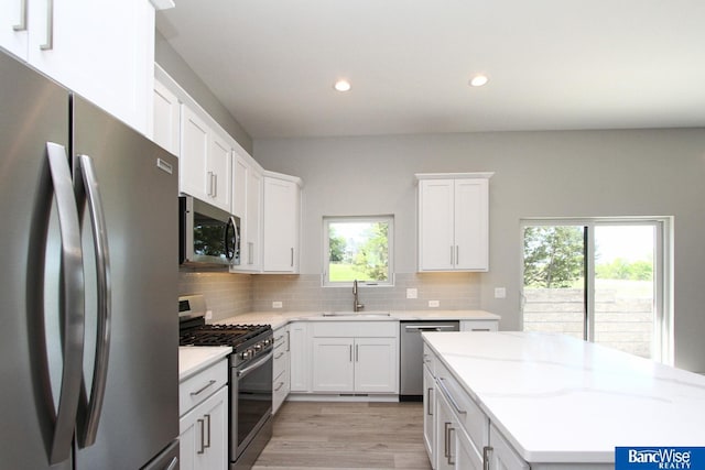 kitchen with decorative backsplash, appliances with stainless steel finishes, white cabinets, a sink, and light stone countertops