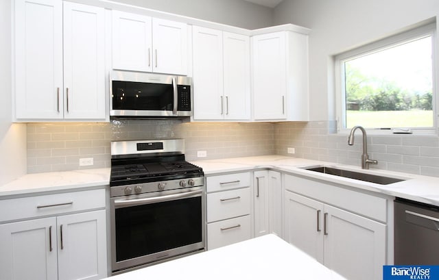 kitchen featuring backsplash, appliances with stainless steel finishes, white cabinets, and a sink