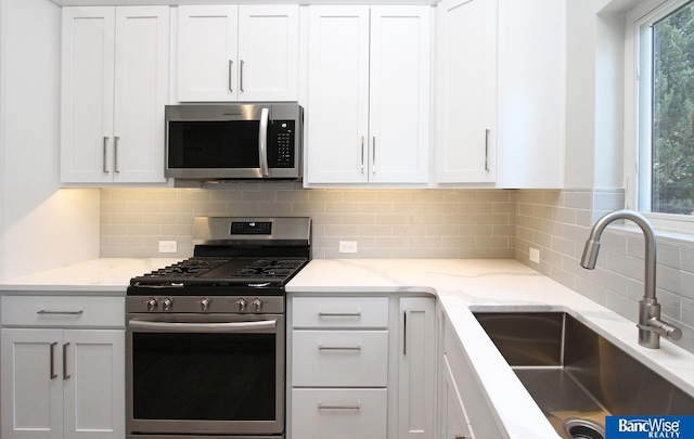 kitchen with white cabinets, light stone counters, appliances with stainless steel finishes, a sink, and backsplash