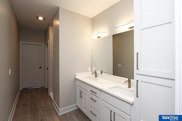 full bath featuring double vanity, a sink, baseboards, and wood finished floors