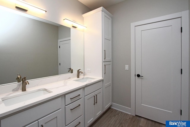 full bathroom featuring double vanity, wood finished floors, a sink, and baseboards