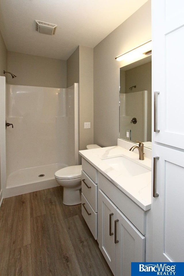 bathroom with visible vents, toilet, vanity, a shower stall, and wood finished floors