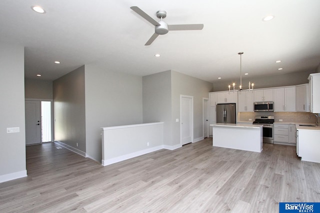 kitchen featuring stainless steel appliances, a sink, white cabinets, light countertops, and pendant lighting