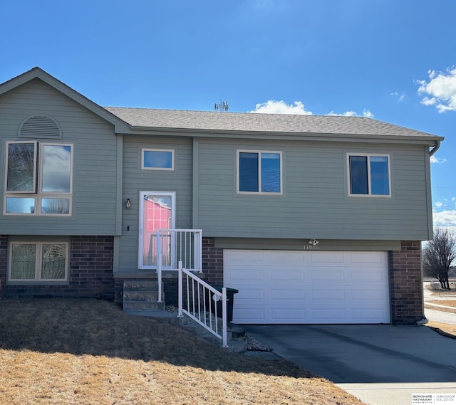 bi-level home featuring brick siding, concrete driveway, a garage, and a shingled roof