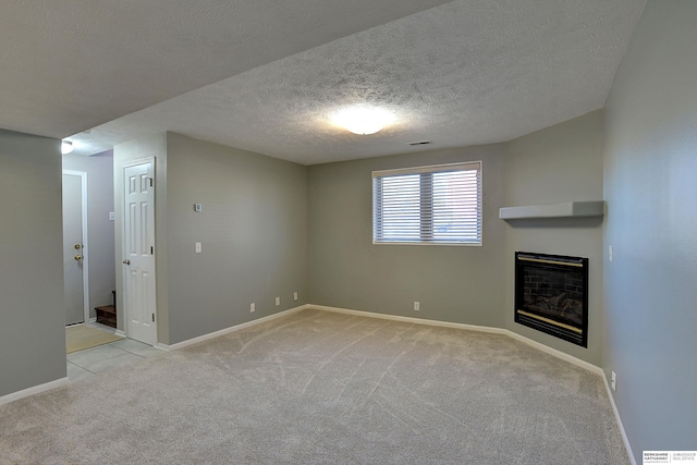 unfurnished living room featuring visible vents, a textured ceiling, a glass covered fireplace, baseboards, and light colored carpet