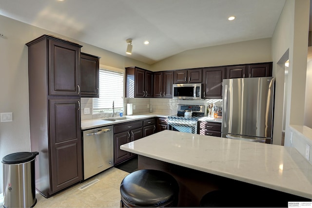 kitchen with a sink, decorative backsplash, dark brown cabinetry, vaulted ceiling, and appliances with stainless steel finishes