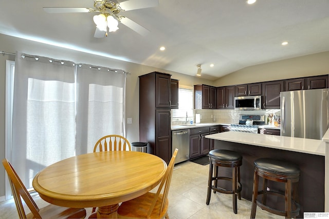 kitchen with dark brown cabinetry, light countertops, lofted ceiling, decorative backsplash, and appliances with stainless steel finishes